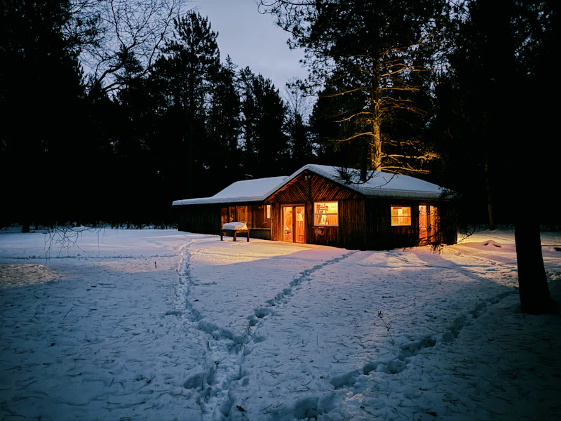 Valaistu hirsimökki lumisessa metsässä illalla